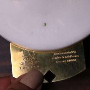 A hand carefully inserts a brass inscription plate into a marble base, highlighting the personalized touch and interactive design of a Turath Kuwait Towers replica.