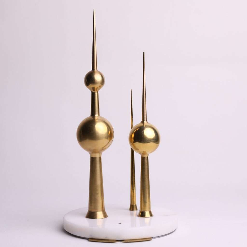 Three gleaming brass replicas of the Kuwait Towers, standing tall on a white marble base, symbolizing heritage and connection. Meaningful Gifting