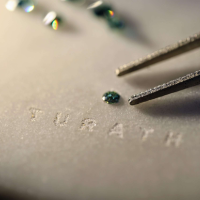 Tweezers carefully placing a sparkling moissanite gem onto a marble base with the Turath logo, highlighting the precious materials used in crafting the Kuwait Towers replicas.